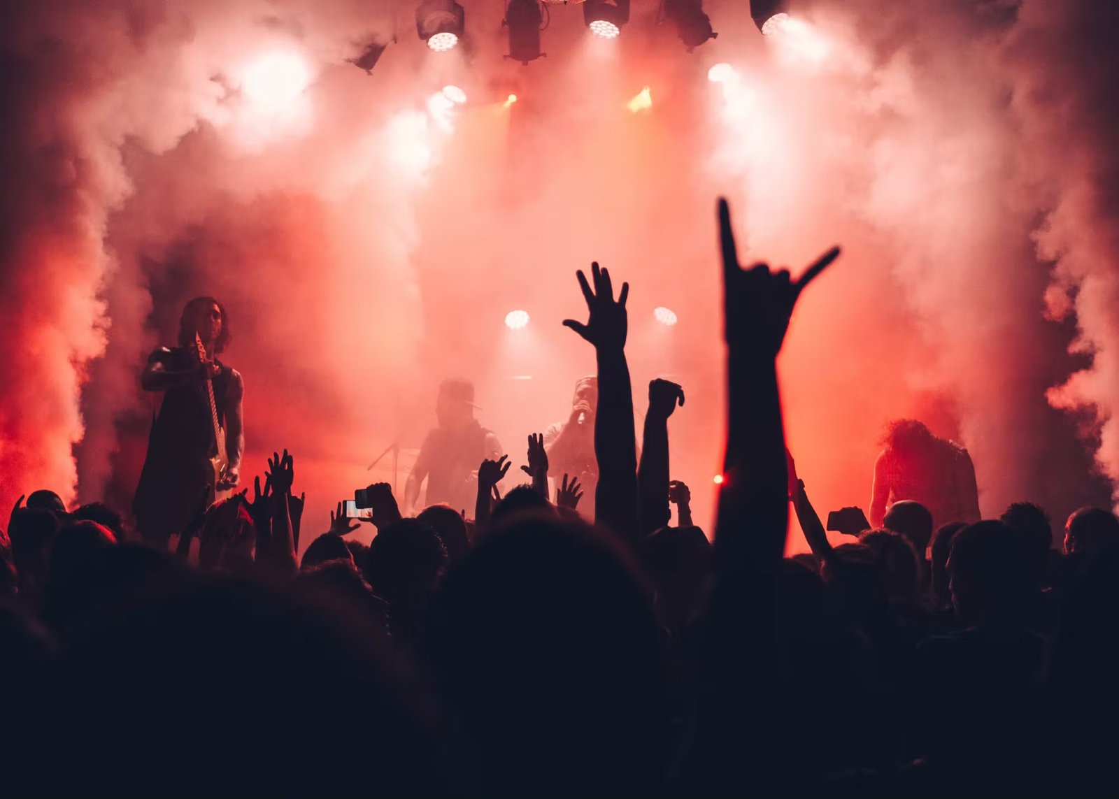 A live band under red stage light and haze, the crowd's hands in the air.