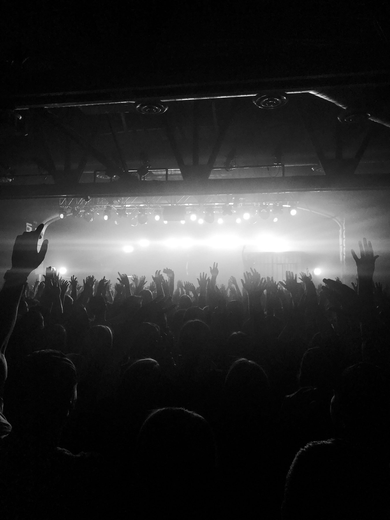 A dark venue with stage lights overhead and a crowd raising hands.