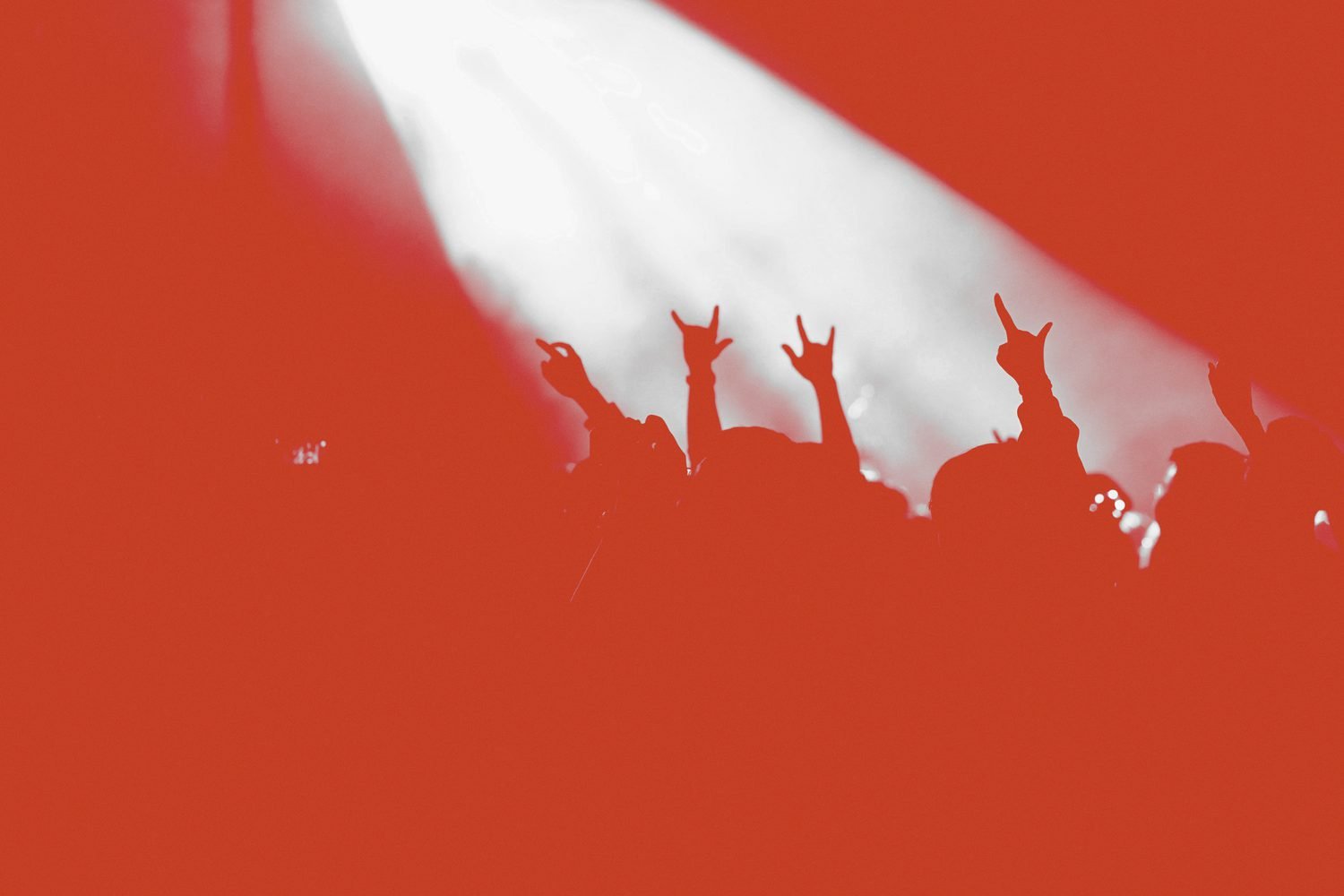 A crowd silhouetted against a flat rust ground, a single white beam cutting down from above.
